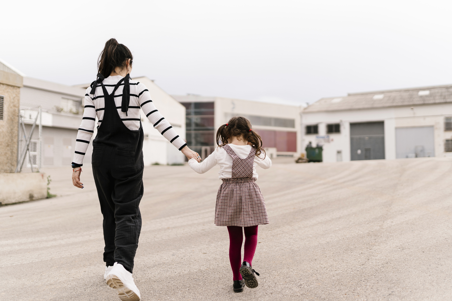 A woman and a young girl walk hand in hand down a paved street.